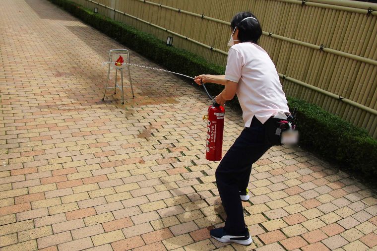 消防署よりお借りした水消火器を使用し、消火器の使用方法を確認しています。 