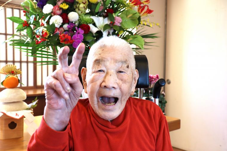華やかなお正月の生花をバックに、ヒュッテ最年長103歳ご入居者の今年も力強い最高の初笑いです！！撮影のためマスクを外しています