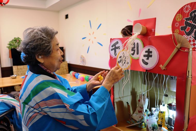 今年の縁日一番人気は手作りの“千本引き”、「どの紐がどの景品に繋がっているのかしら？仕掛けもすごいわねぇ」と、ワクワクの眼差しです！